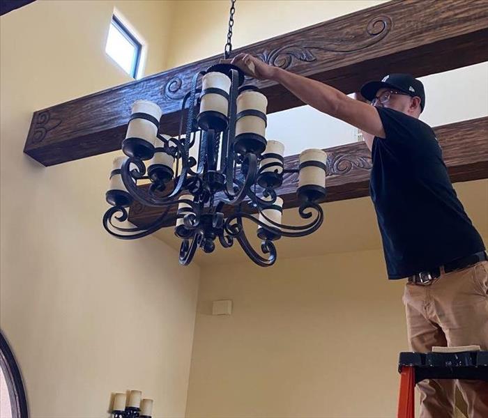 male SERVPRO employee on ladder cleaning off chandelier 