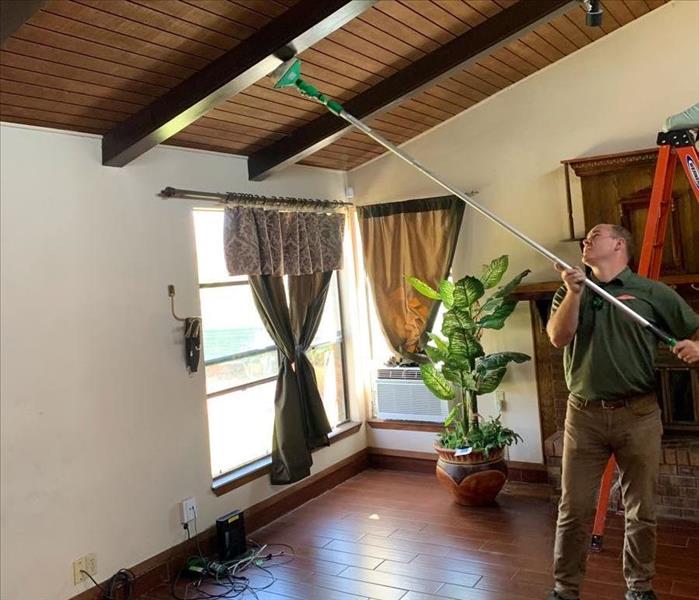 male SERVPRO employee using long brush to clean ceiling 